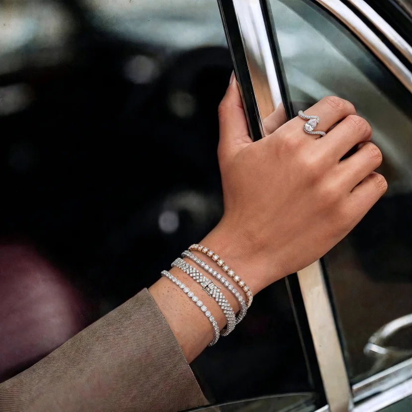 Hand wearing stacked diamond bracelets and statement ring near car door